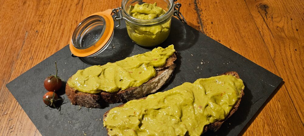 Deux tranches de pain grillé tartiné avec la tartinade d'avocat à la tomate. Elles sont posées à côté du pot de tartinade, sur un plat en ardoise.