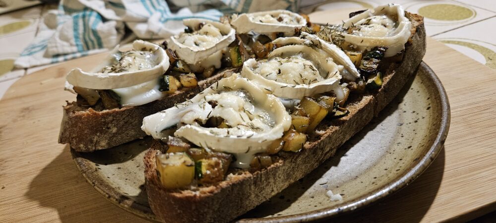 Deux tartines aux courgettes, fromage de chèvre, miel et thym déposées sur une assiette.